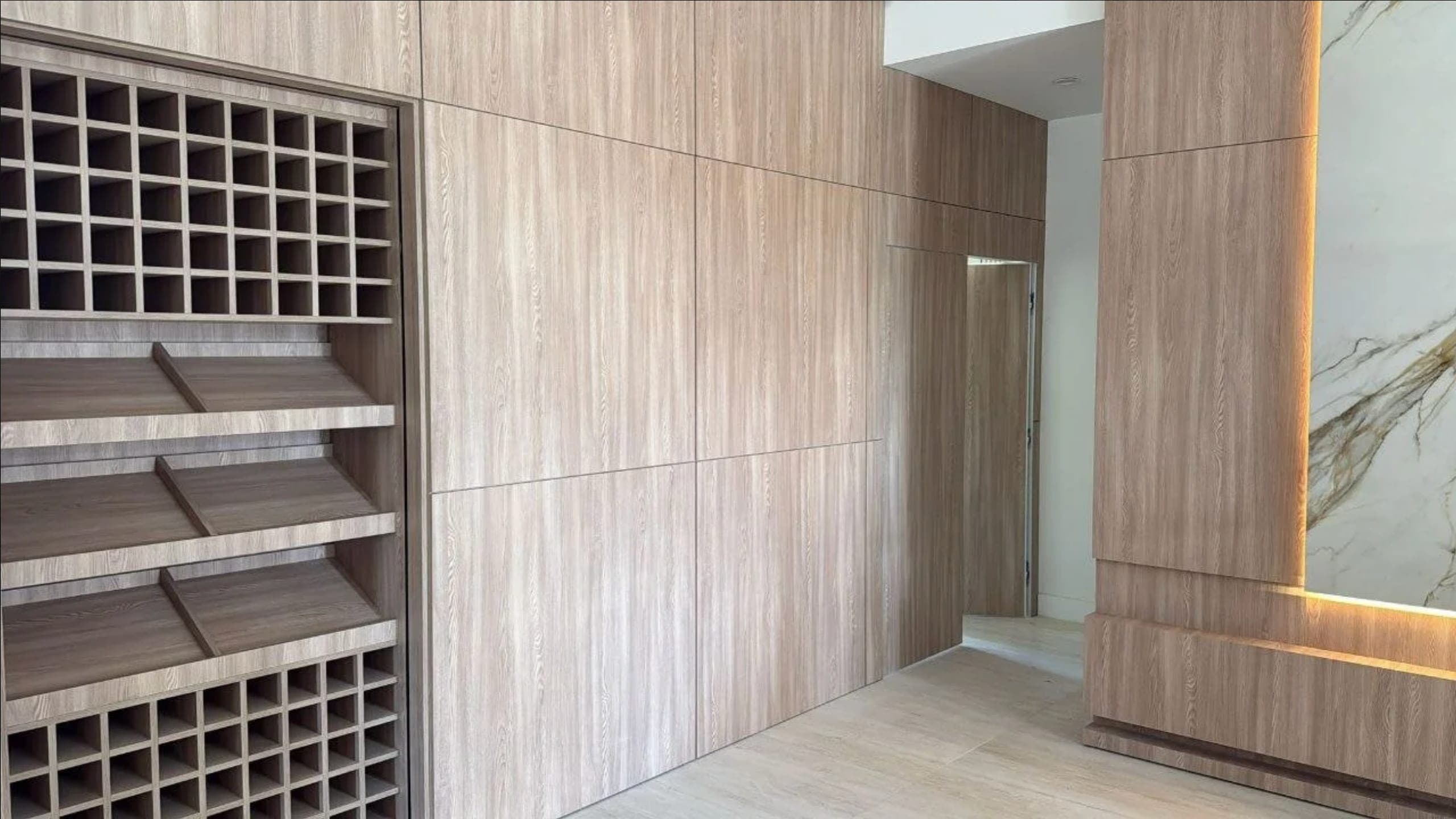 Wood-paneled wall with integrated wine storage, a concealed door, and a backlit marble accent
