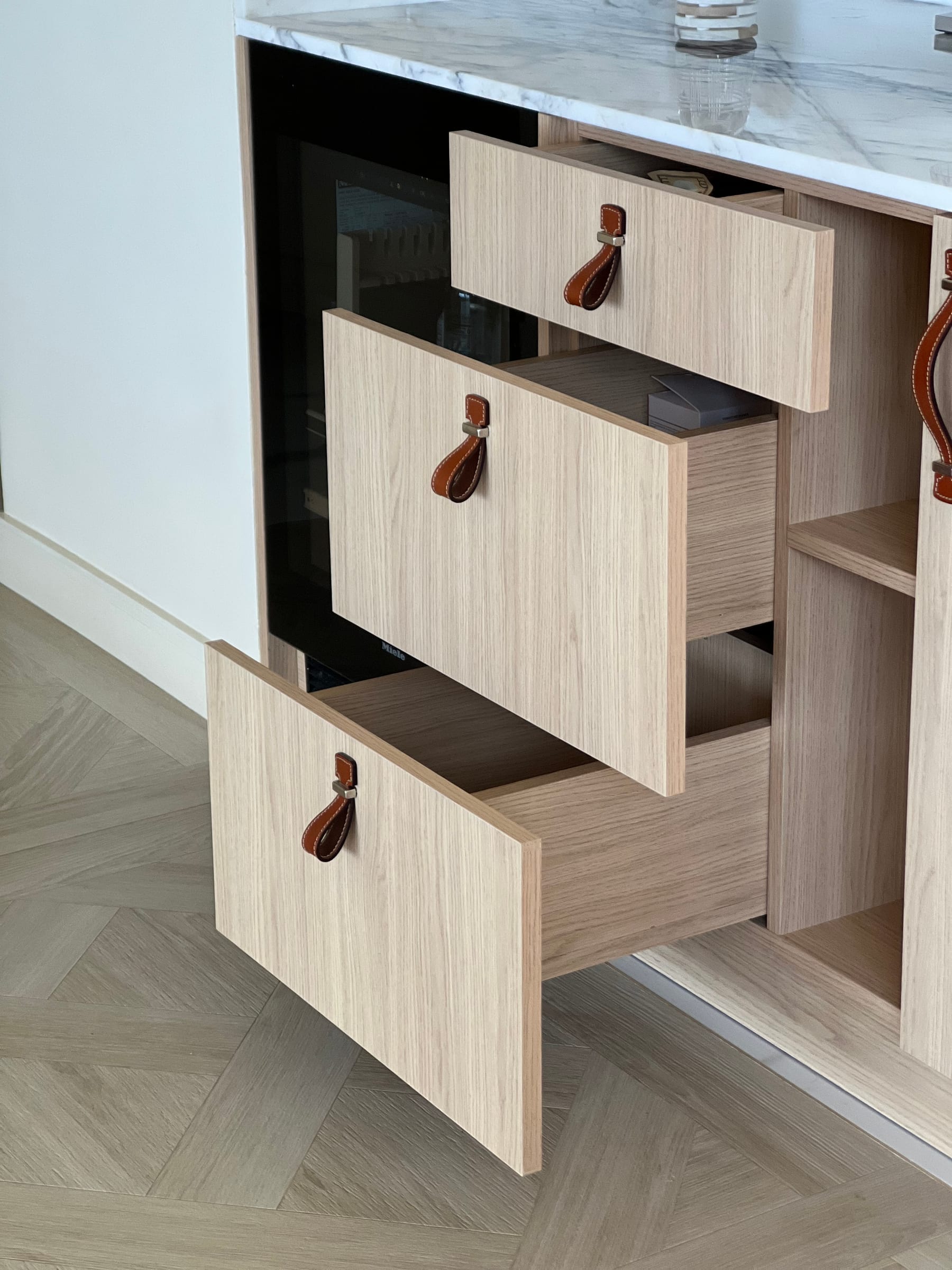 Oak drawers with stitched-leather pulls beneath a Calacatta marble countertop — Acqualina residence
