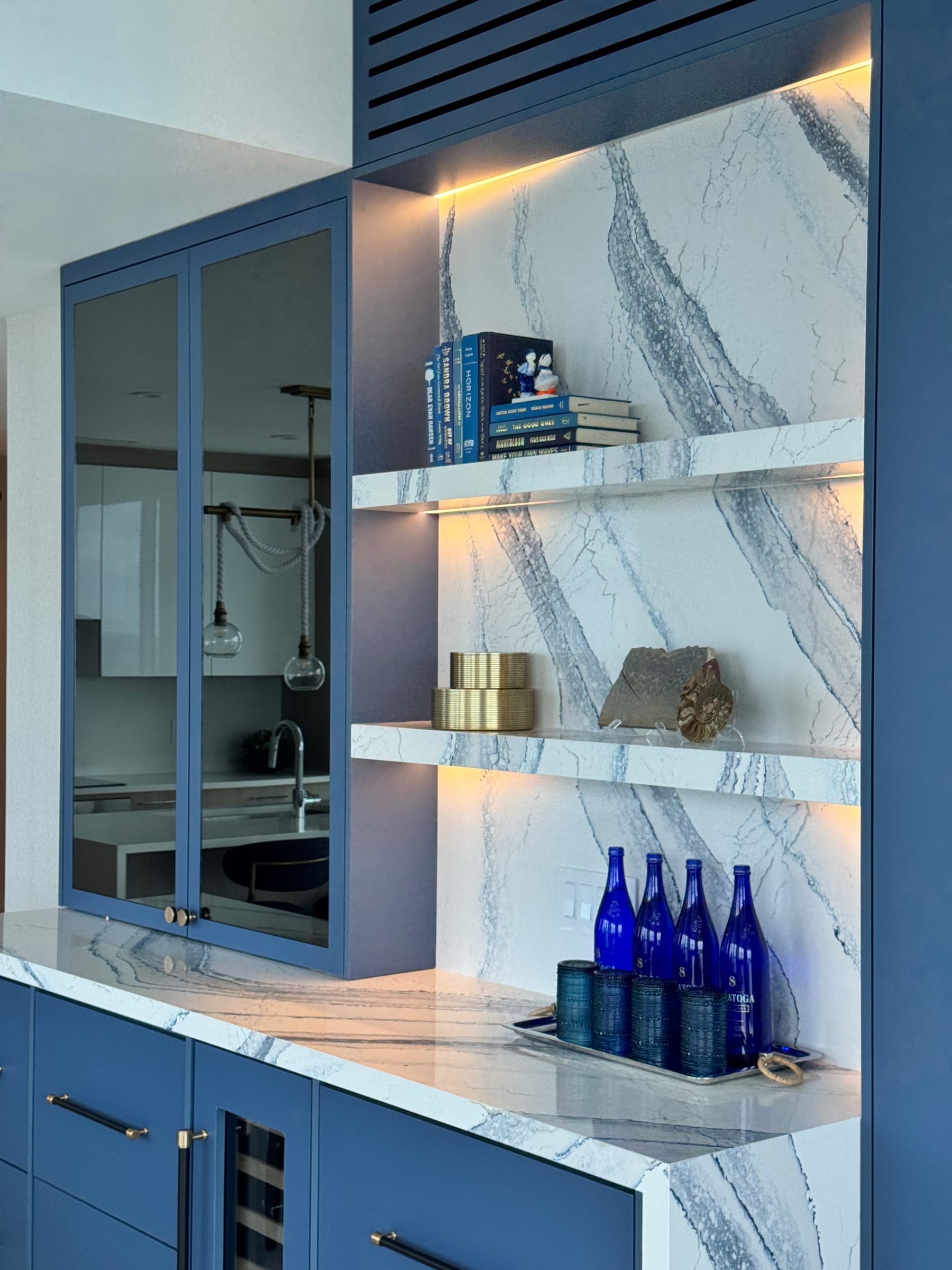 Navy-blue built-in bar with backlit quartzite shelves and glass-front cabinets — Selene oceanfront residence